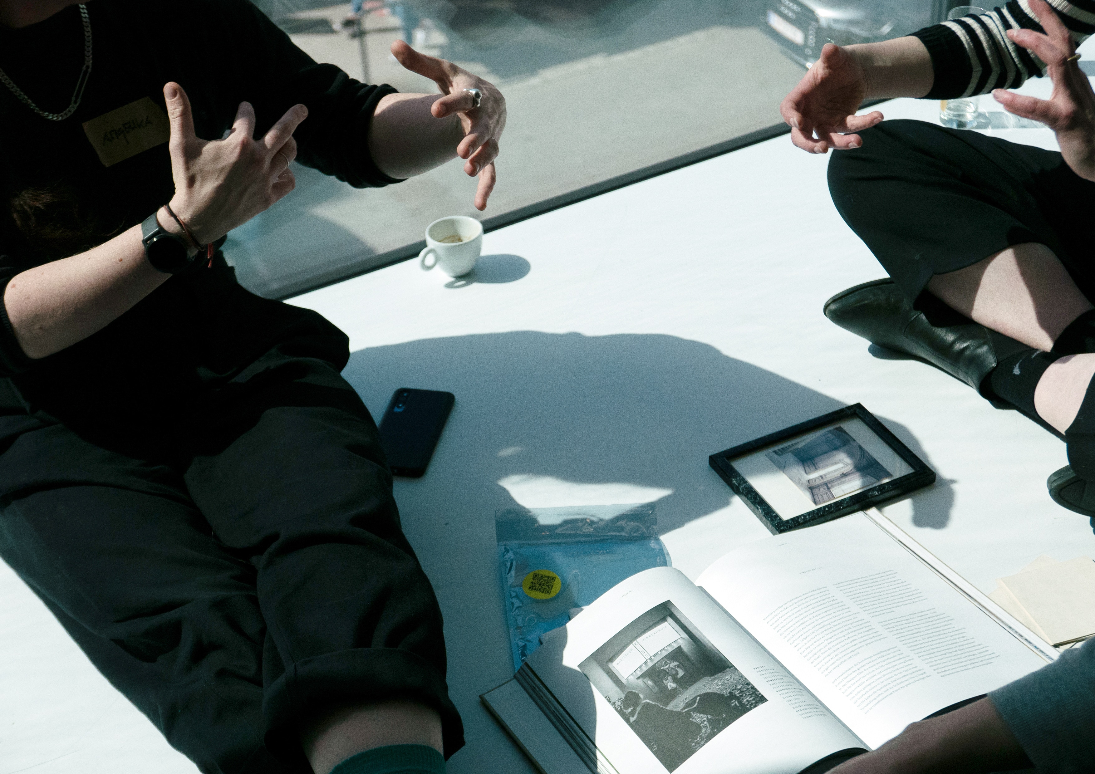 Hands gesturing in conversation above an open book and a framed photo on the floor asphalt kollektiv