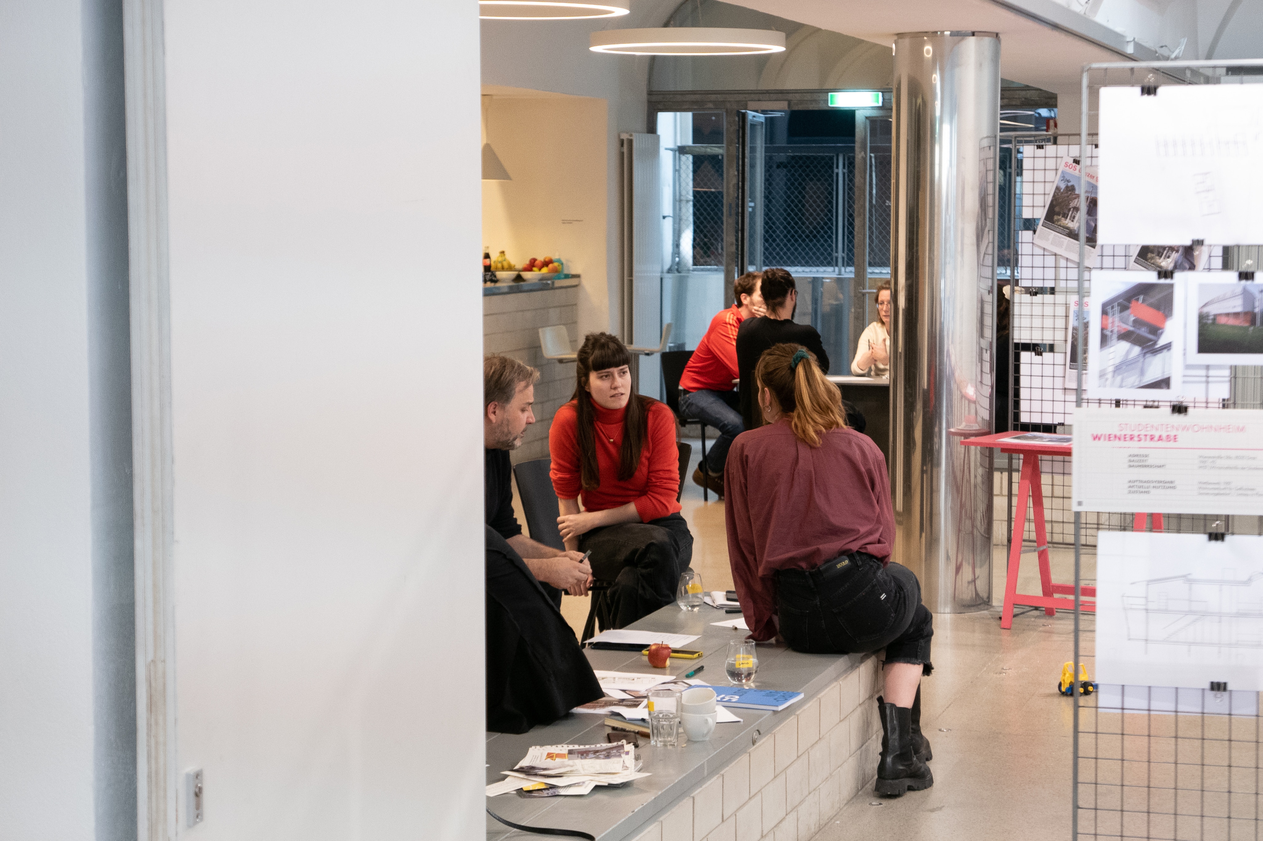 View into a workshop space: participants on a bench, drawings pinned to a grid panel asphalt kollektiv