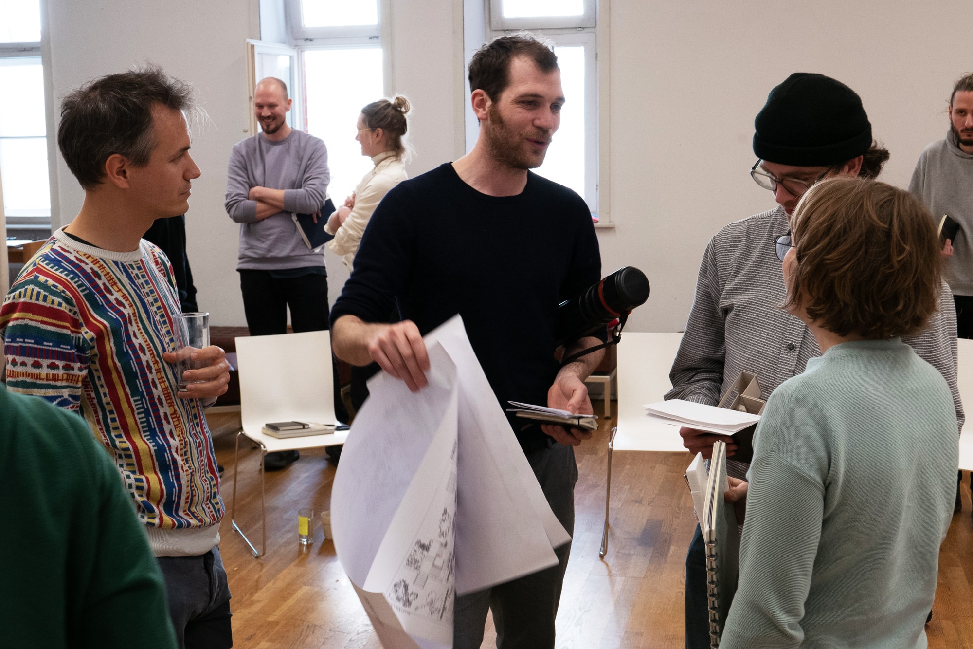 Participants discussing in a workshop room, one holding a large sheet of drawings asphalt kollektiv