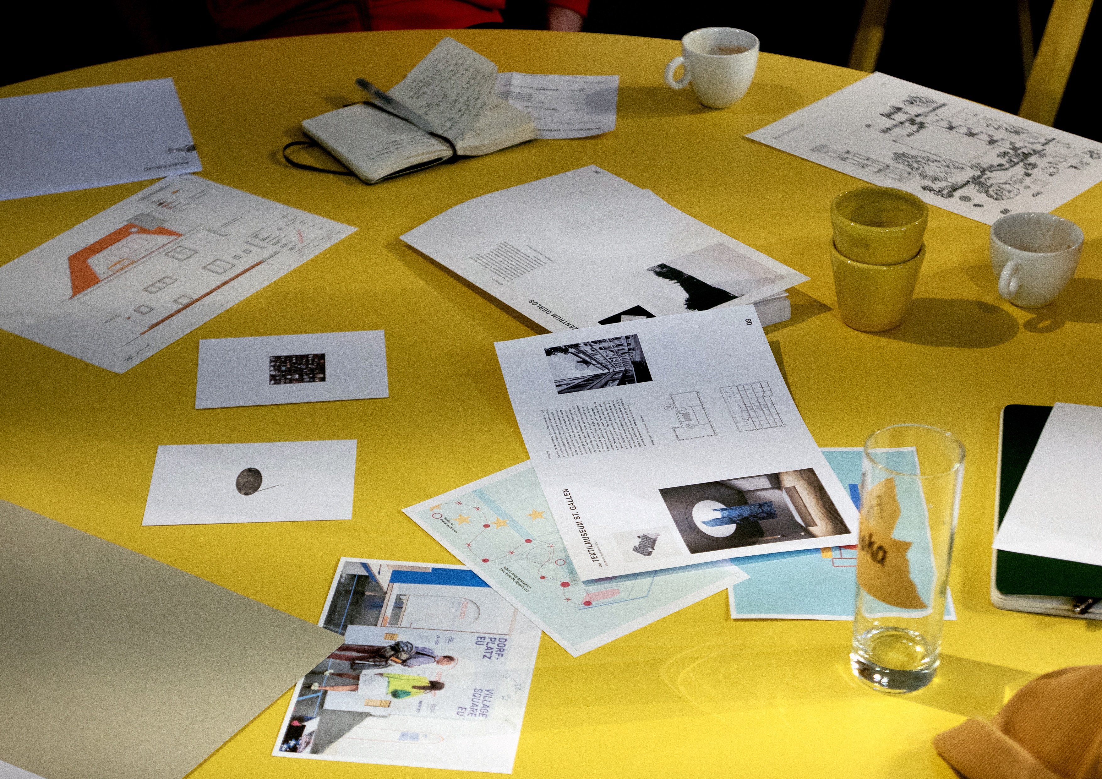 Yellow table covered with drawings, photos, notebooks and cups brought by participants asphalt kollektiv