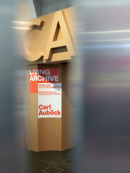 Eingangsportal: Kartonbuchstaben „CA“ über dem Ausstellungsplakat „Living Archive“ mit dem Namen Carl Auböck asphalt kollektiv