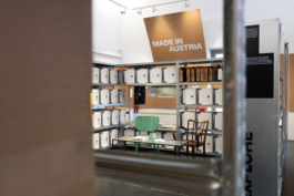 Bereich „Made in Austria“: Metallregale mit Archivboxen, davor ein grüner Stuhl und ein Holzstuhl an einem Tisch asphalt kollektiv