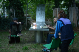 Performers at the table, the movable half raised upright as a vertical mirror behind them asphalt kollektiv