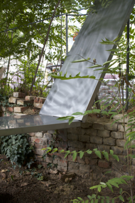 Raised mirror half leaning over the old brick wall at the fence, reflecting the foliage asphalt kollektiv