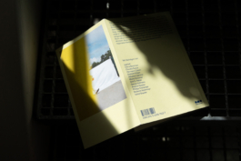 Umbauhof-Buch mit gelbem Umschlag, eingelegtem Foto und Liste der beitragenden Autor:innen asphalt kollektiv