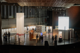 Theaterbühne mit den Beiträgen der Ausstellung, darunter der marmorierte Würfel, Besucher:innen dazwischen asphalt kollektiv