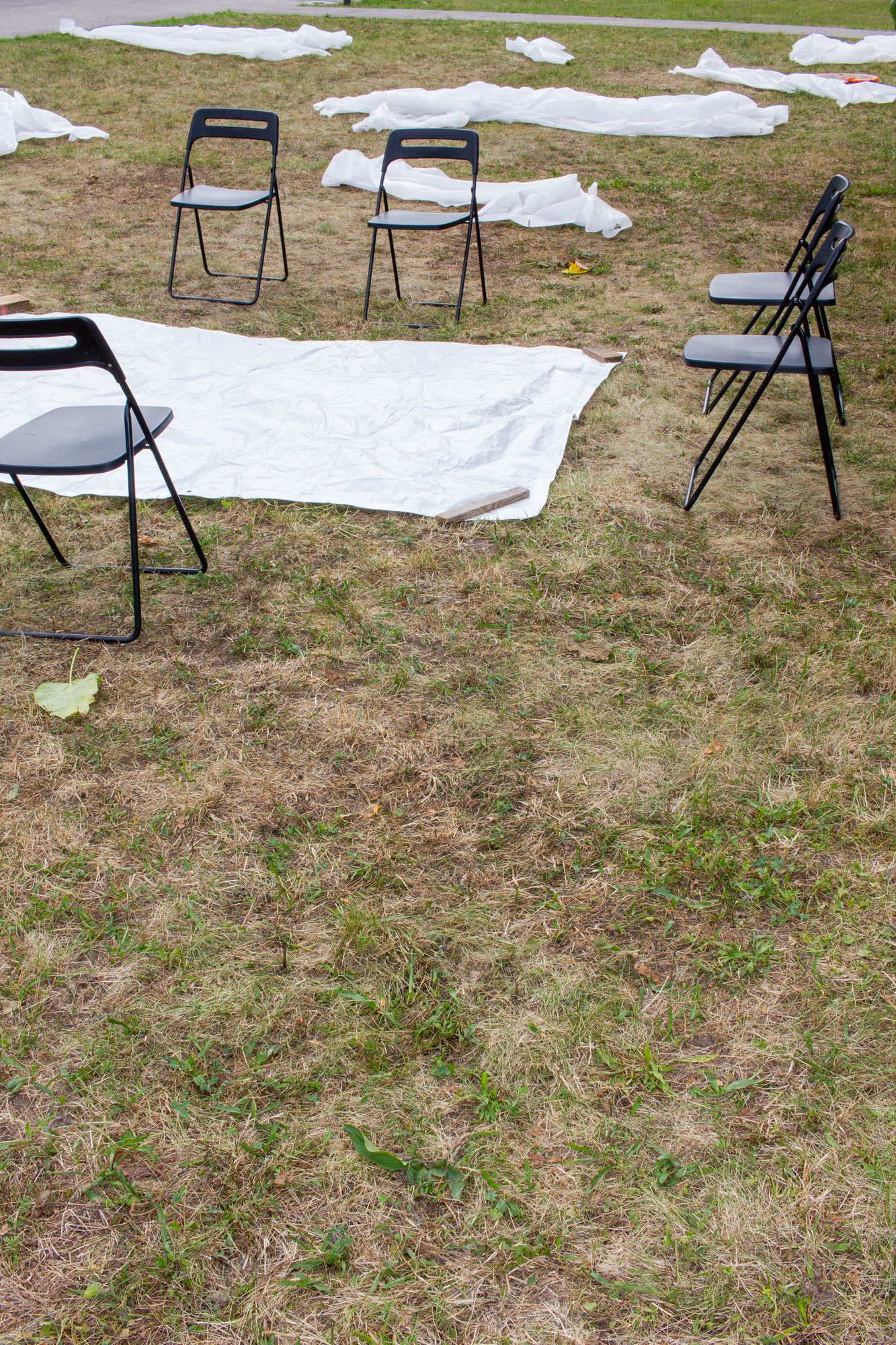 Folding chairs and white tarps spread across a dry lawn, an outdoor workspace for the summer school asphalt kollektiv