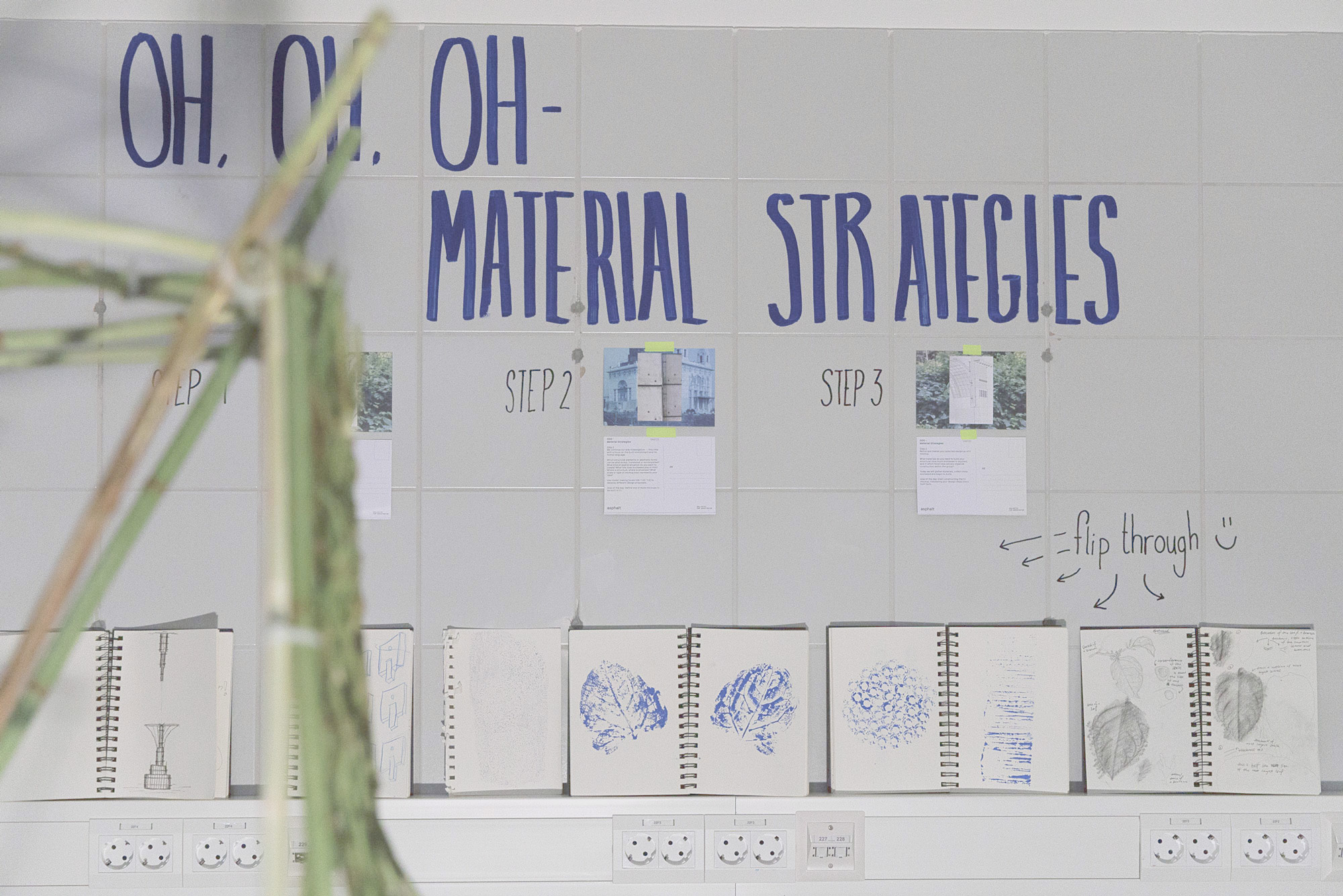 Exhibition wall with the hand-painted title “Oh, Oh, Oh – Material Strategies”, task cards for steps 1–3 and open sketchbooks with leaf prints and drawings asphalt kollektiv