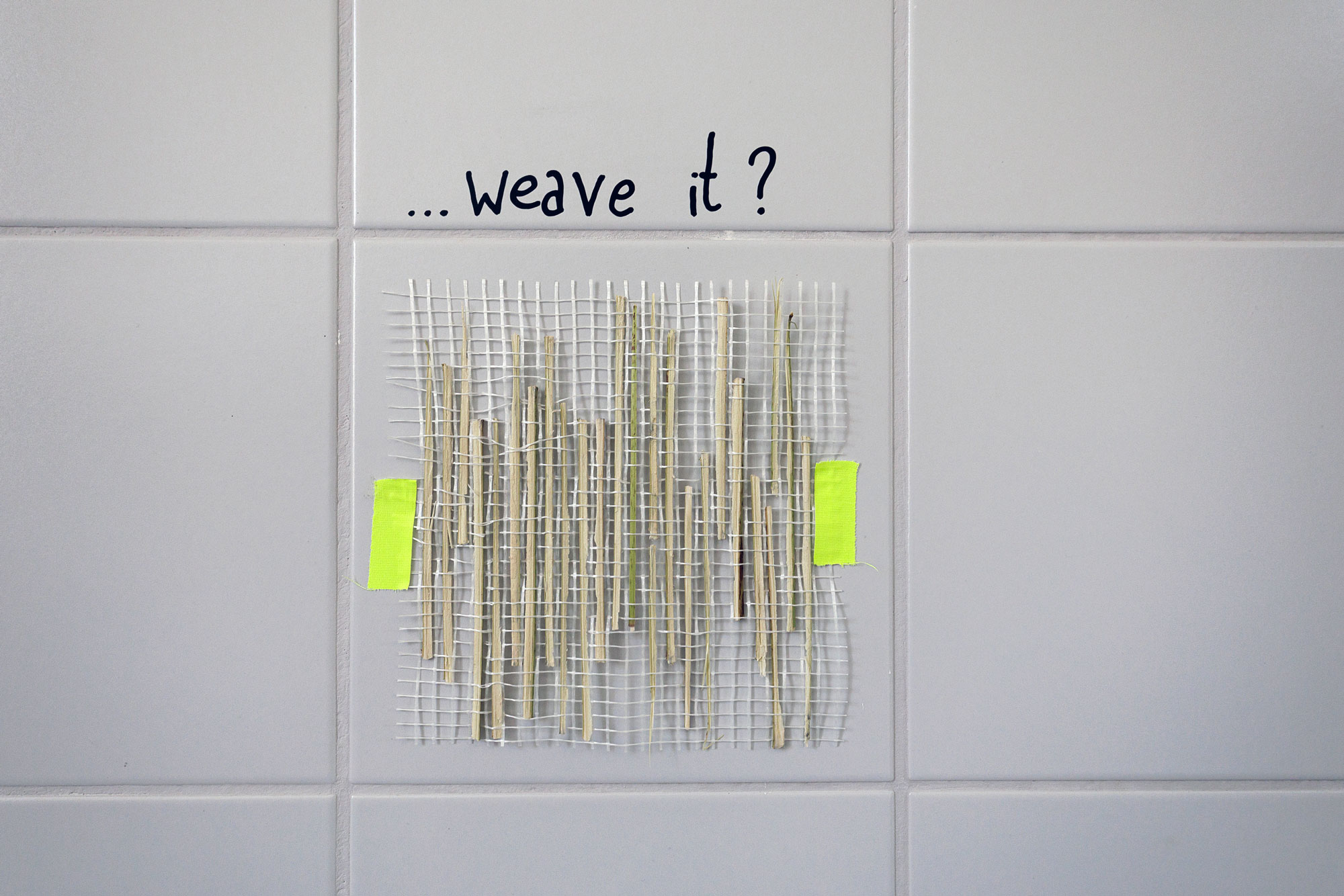Strips of split knotweed stalk woven into a white fibreglass mesh, taped to a tiled wall below the handwritten question “…weave it?” asphalt kollektiv